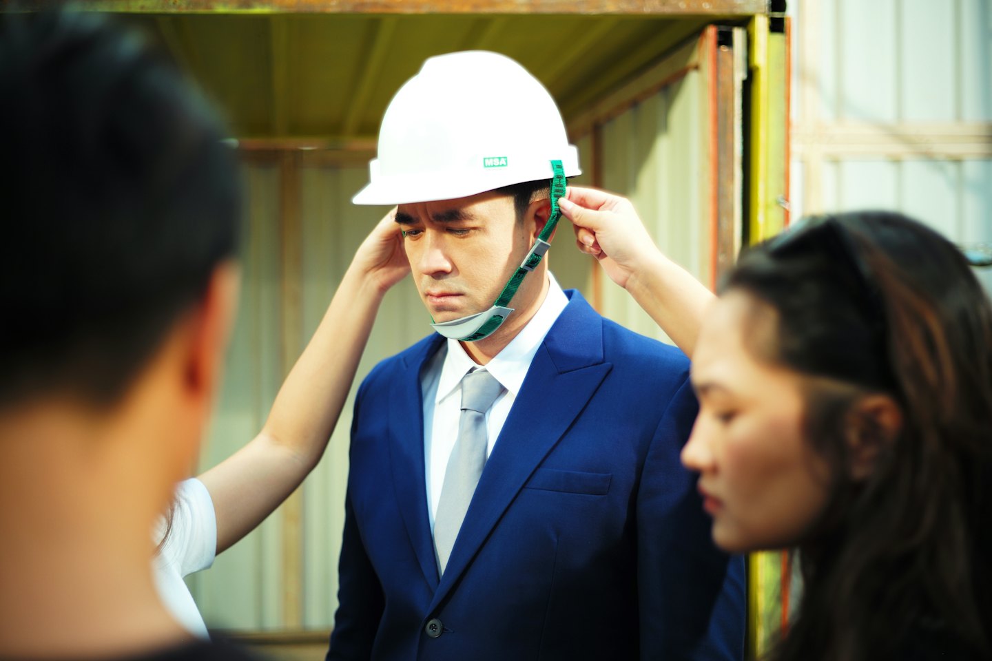 Due operai allacciano un casco di sicurezza sulla testa di un uomo.
